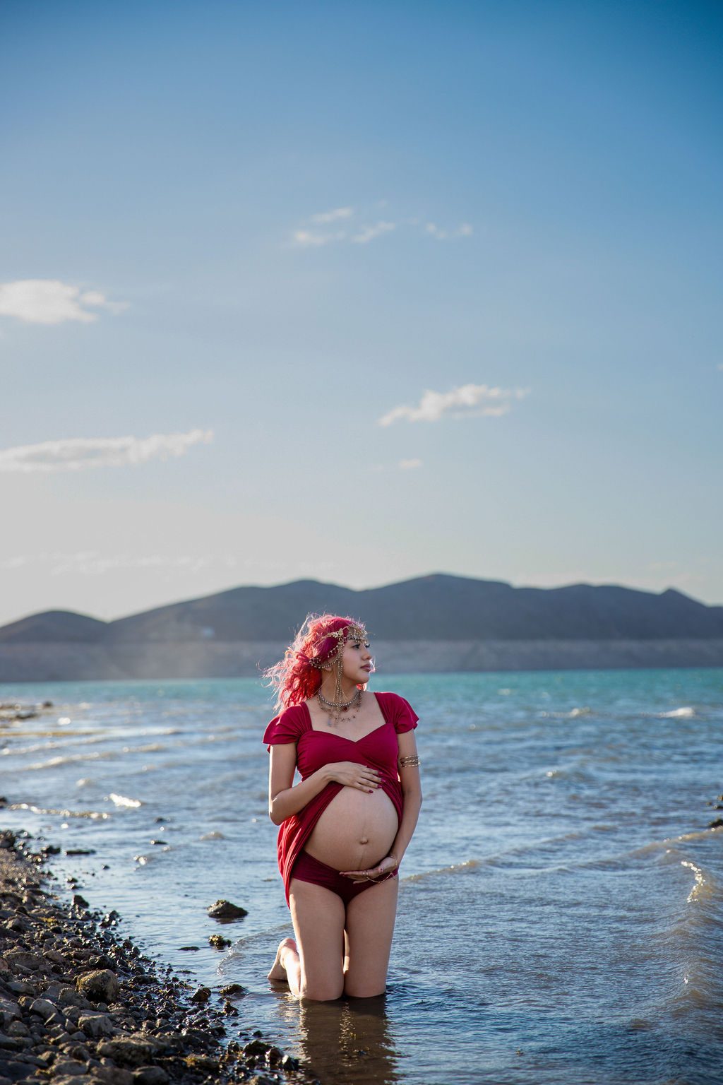 Maternity photography at Lake Mead near Las Vegas — expecting mother kneeling in the shallows at golden hour