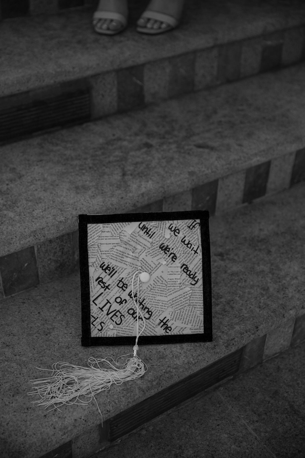 Black and white senior photography detail — decorated graduation cap resting on stone steps