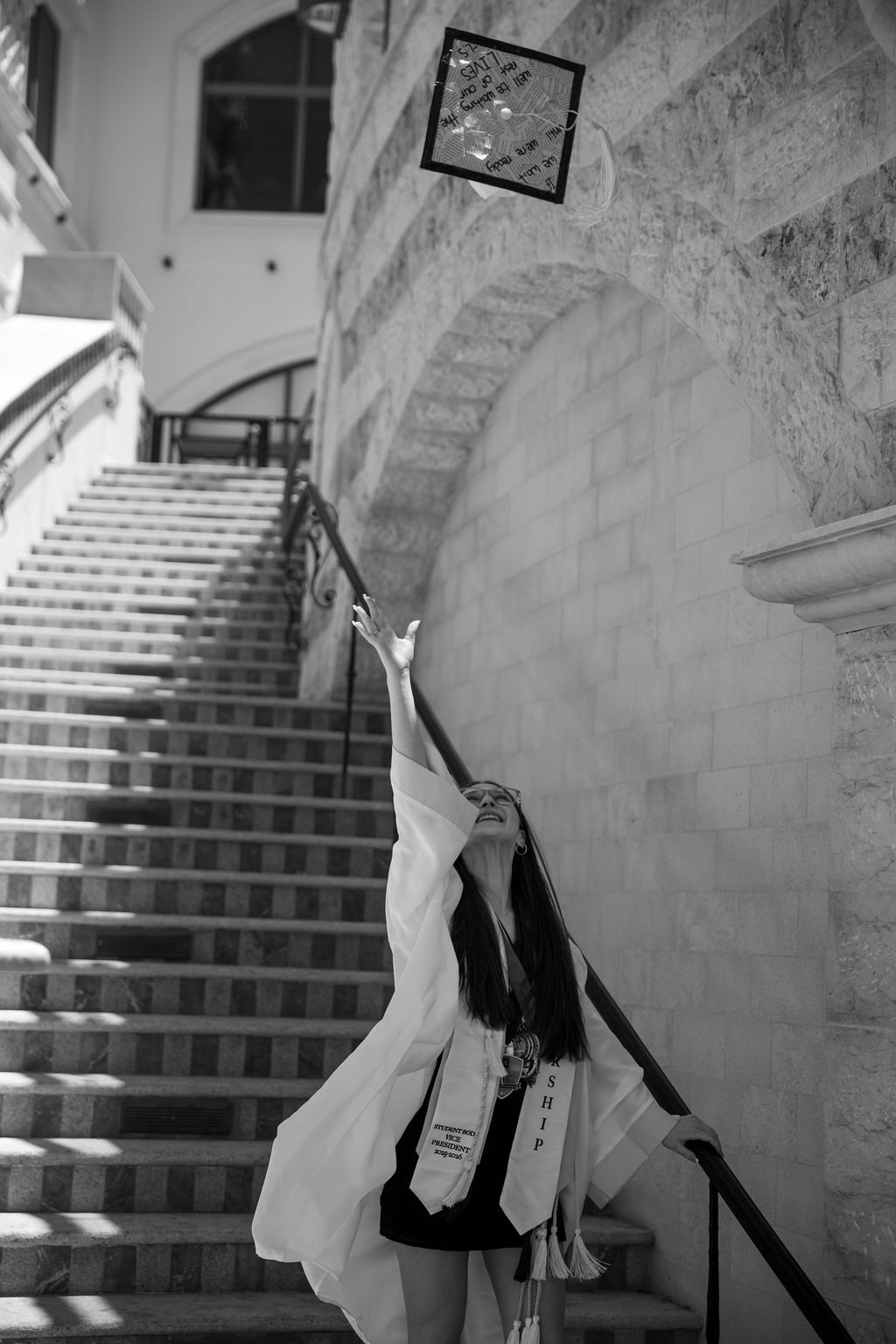 Black and white senior photography in Las Vegas — graduate throwing her cap on a staircase