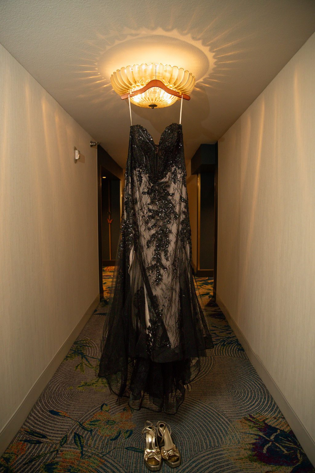 Wedding detail photography in Las Vegas — black lace gown hanging in a hotel hallway